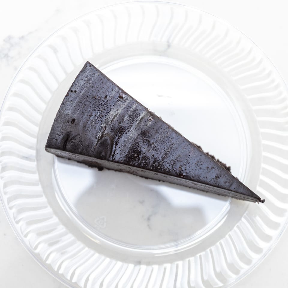 Slice of dark chocolate cake on a white ridged glass plate.