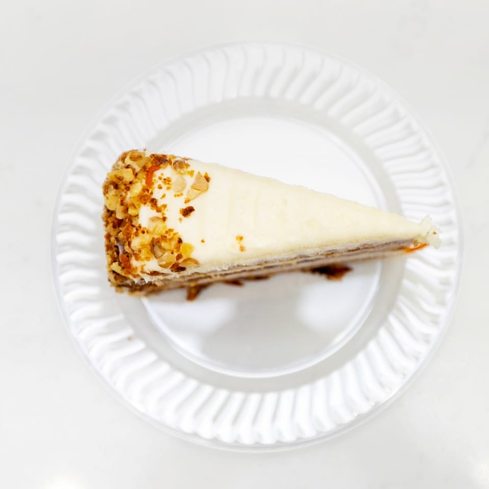 Triangular slice of cream-filled cake topped with crushed nuts on a white ridged plate.
