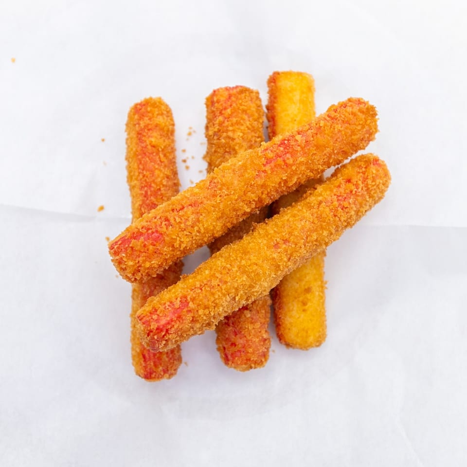 Several golden-brown breaded snack sticks with reddish seasoning arranged on white paper.