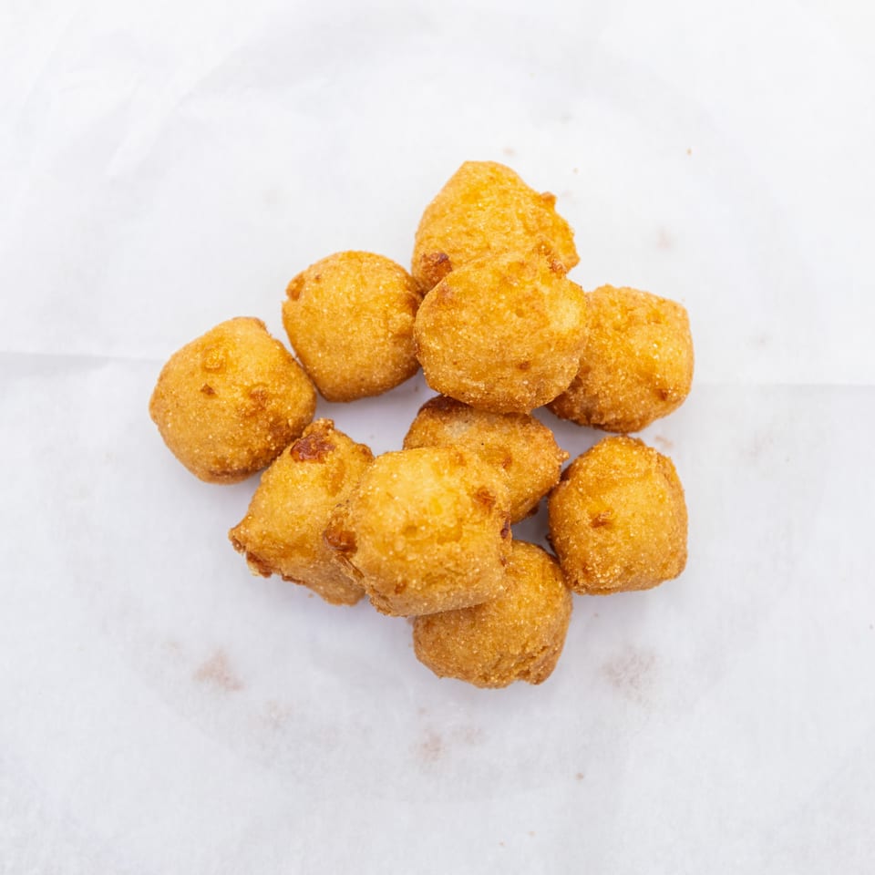 Pile of golden-brown fried fritters arranged on white parchment paper.