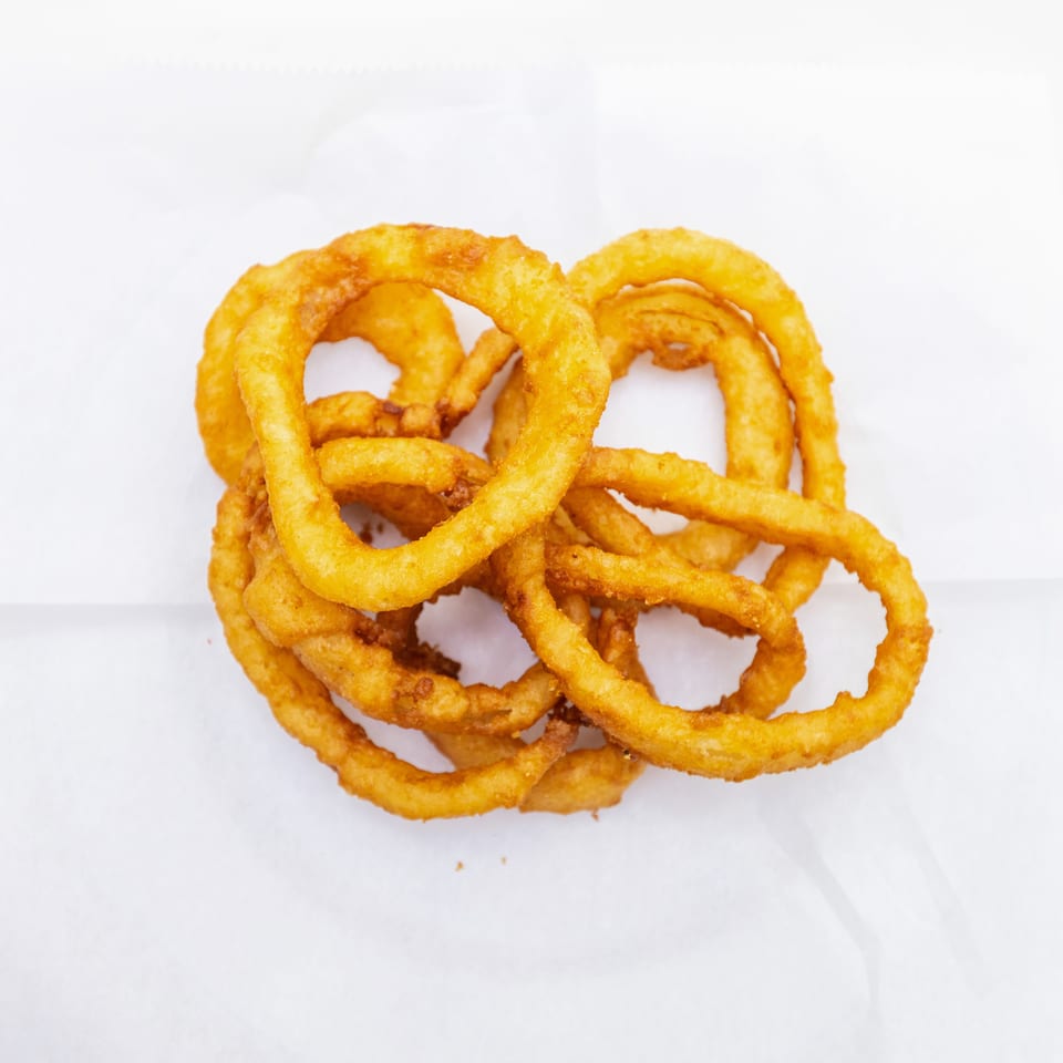 A pile of golden-brown crispy onion rings rests on white paper.