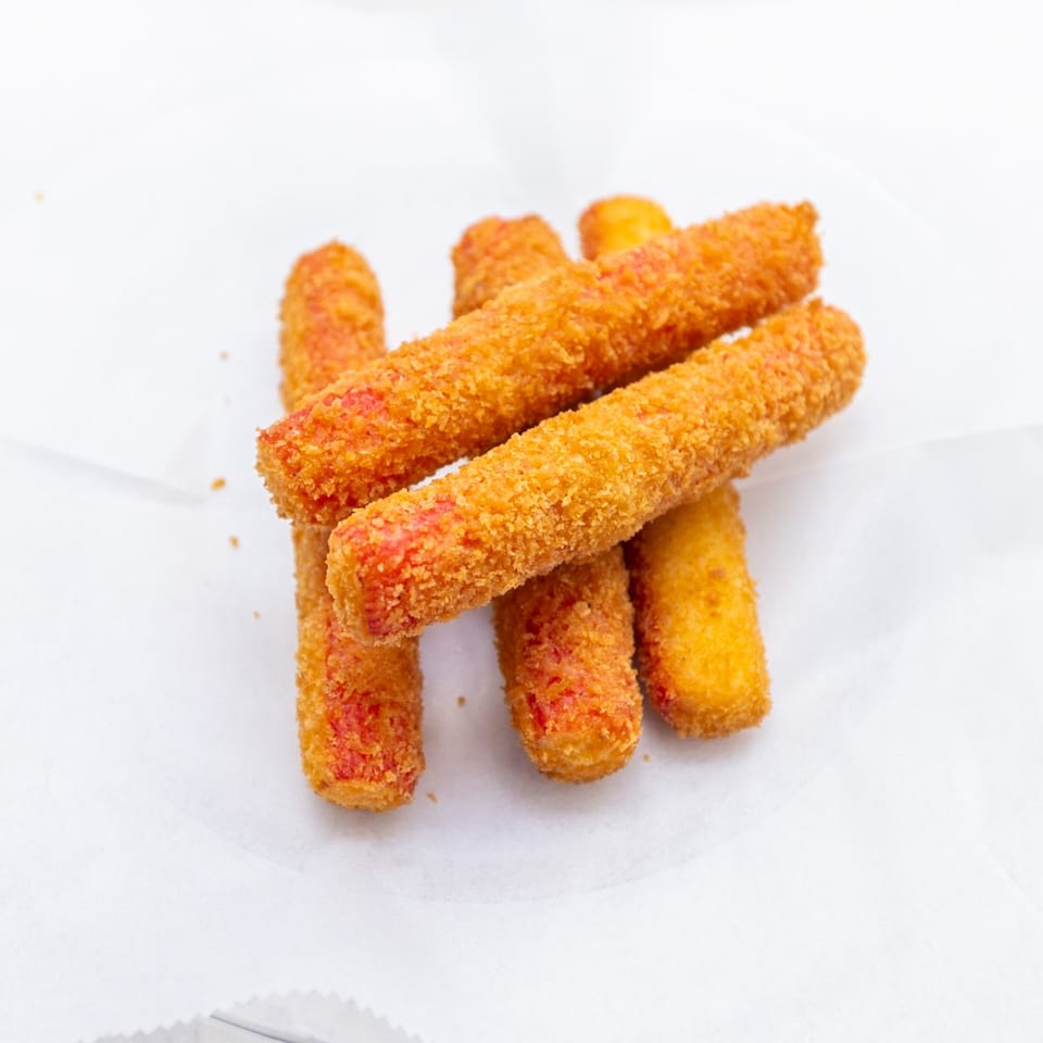 Pile of golden breaded mozzarella sticks with reddish seasoning on white paper.