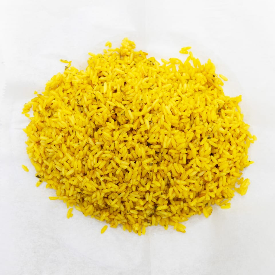 A mound of bright yellow seasoned rice sits on a white plate.
