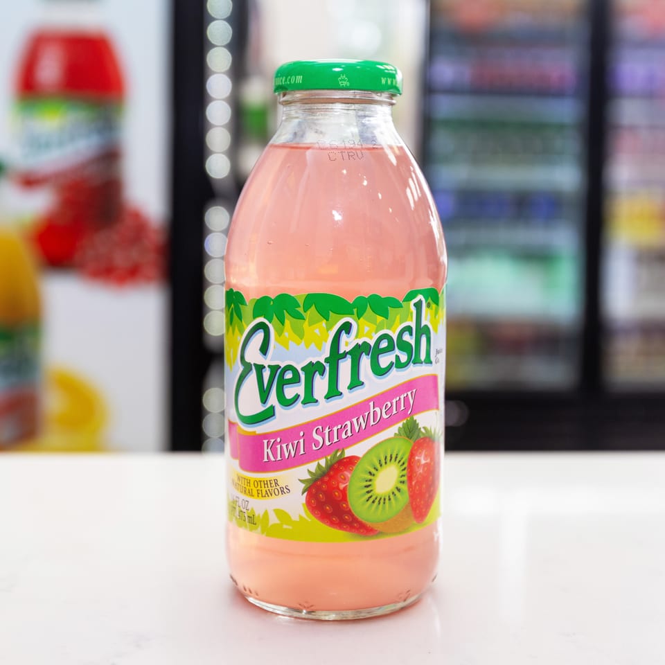 Bottle of pink Verifresh kiwi strawberry drink on a white counter, with colorful beverage bottles blurred in the background.