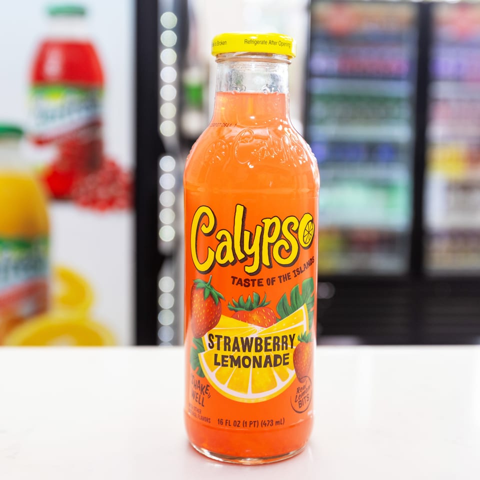 Bottle of Calypso strawberry lemonade displayed on a counter in front of a refrigerated beverage case.